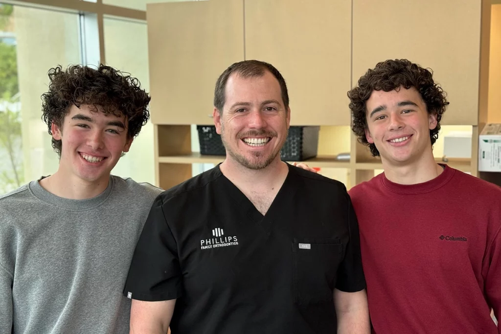 Dr. Joseph Phillips, orthodontist, with two smiling teenage patients showing off their perfect smiles.